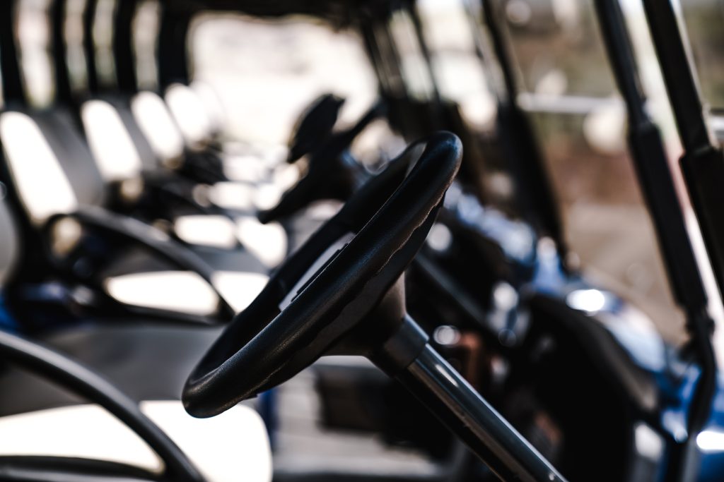 A detailed close-up of multiple golf cart steering wheels aligned in a row outdoors.